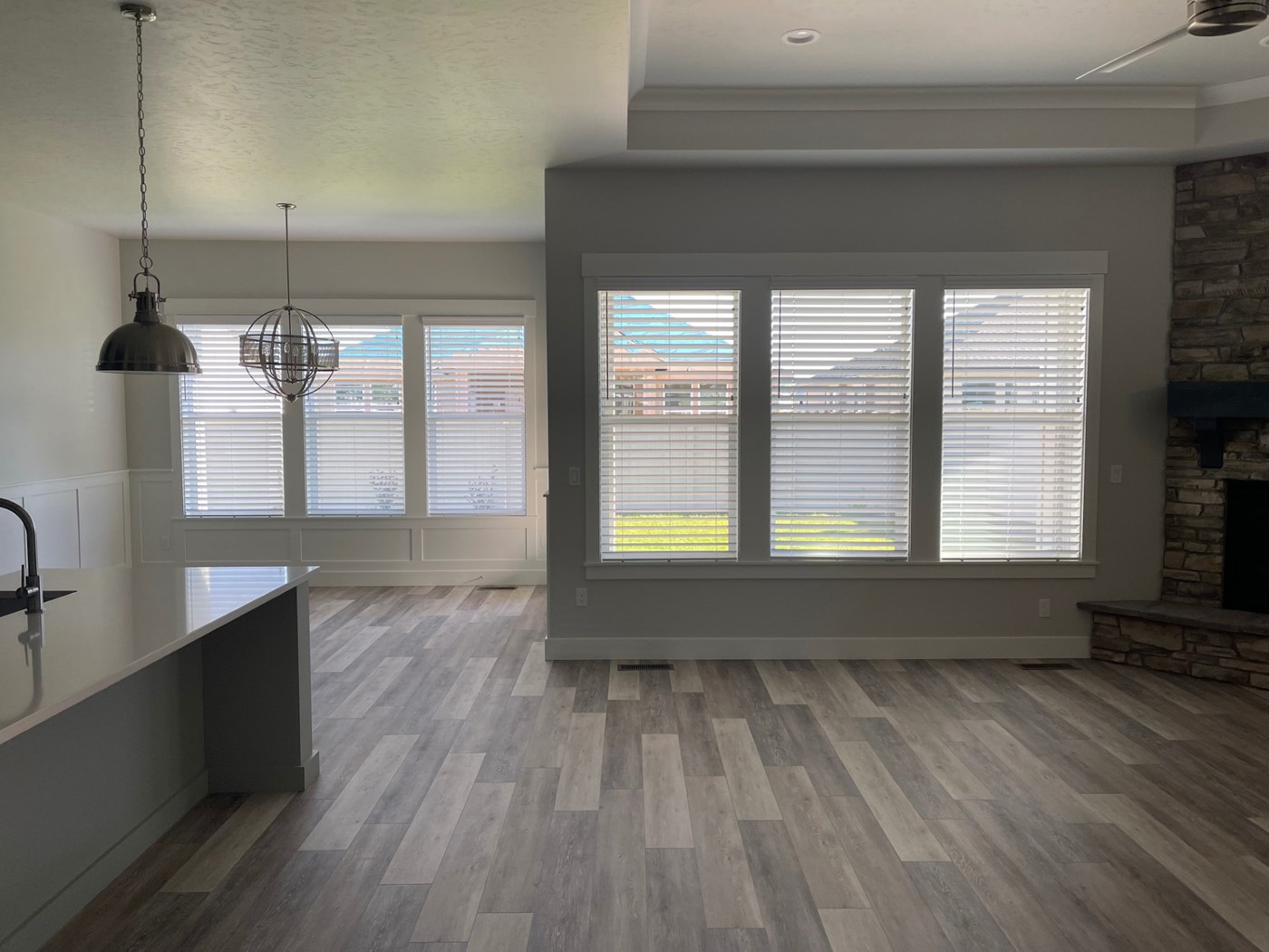 White faux wood blinds across multiple windows in an open kitchen and great room